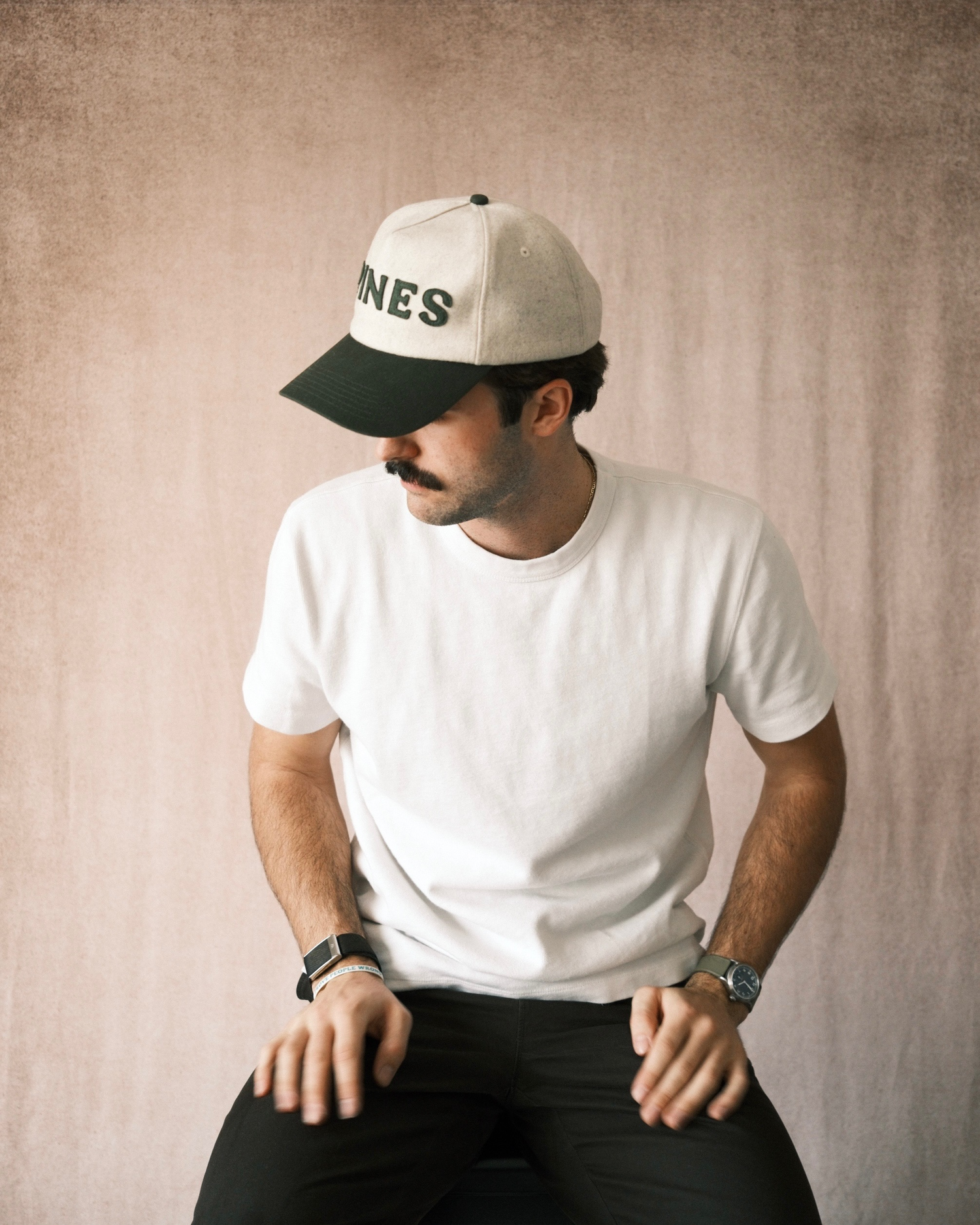 Man wearing a white cap and white t-shirt against a beige background